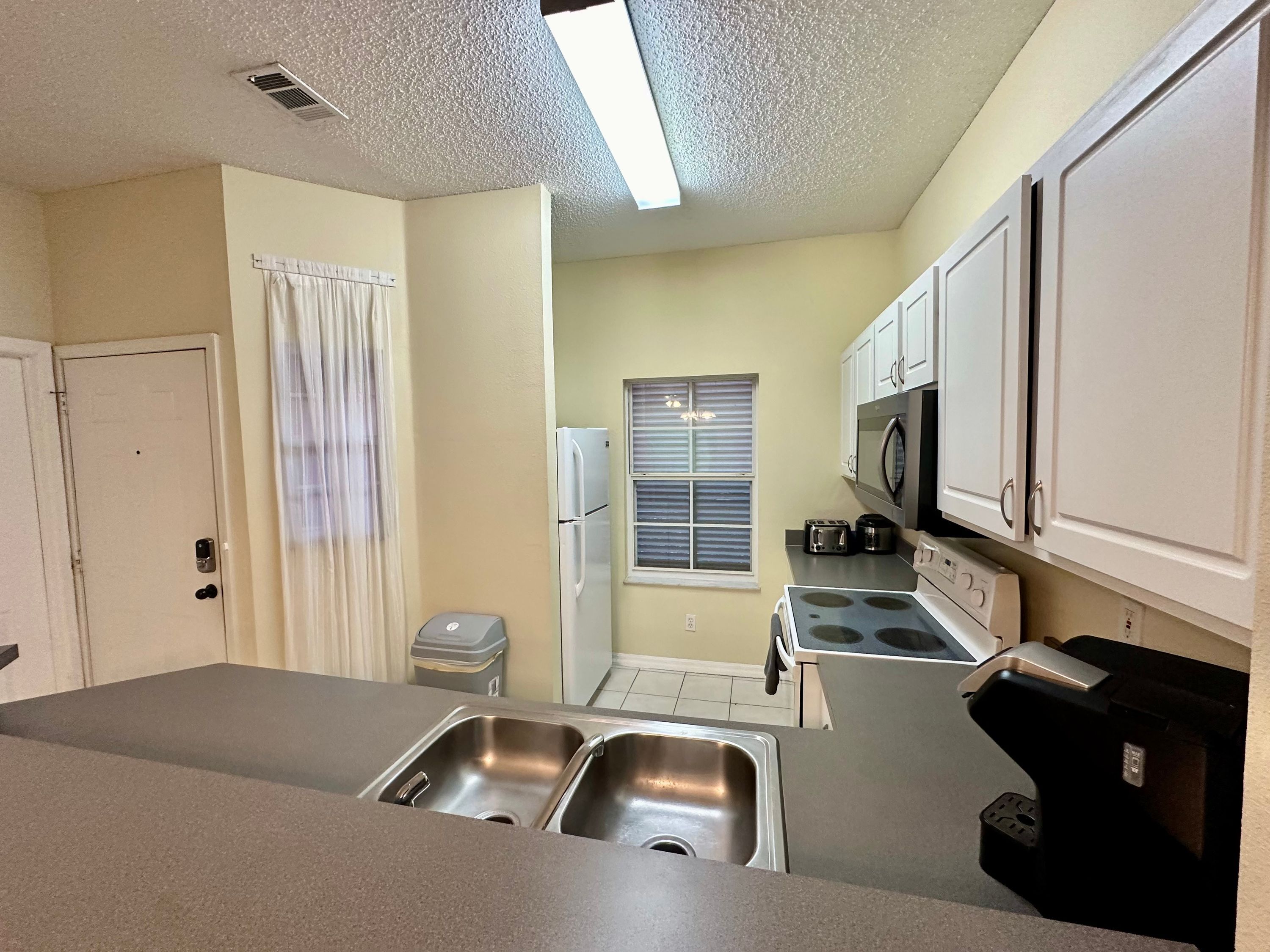 A compact kitchen with a double sink, a refrigerator, a microwave, and a stove.