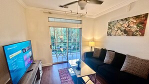 A living room with a TV, a ceiling fan, a sofa, a coffee table, and a view through a glass door to an outdoor area.