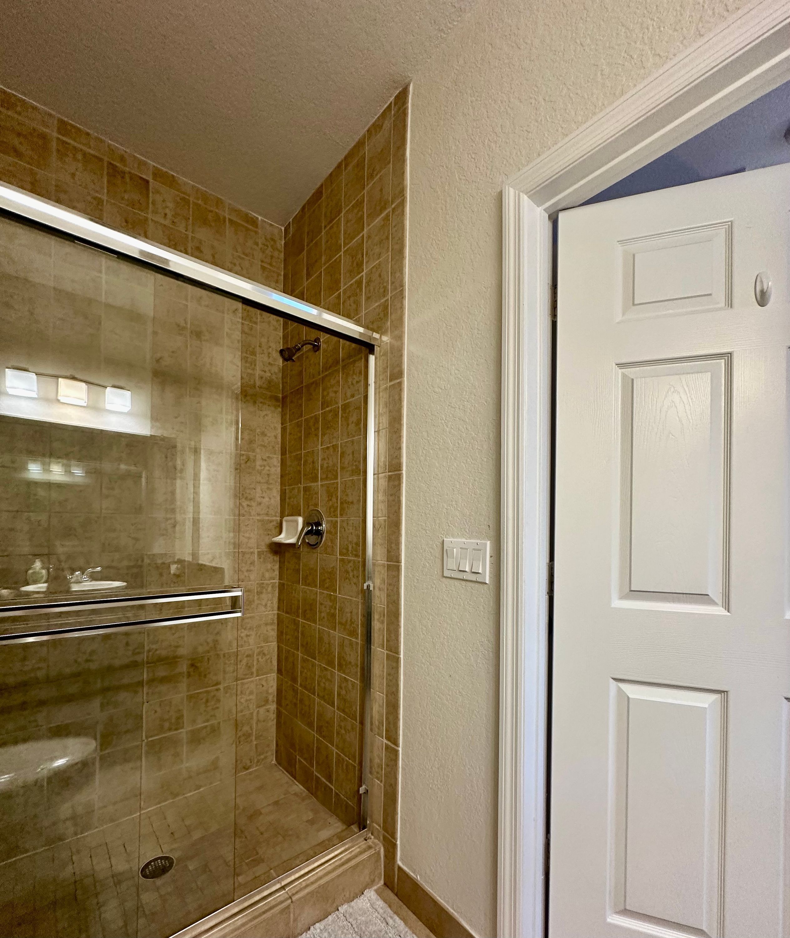 A bathroom with a glass-enclosed shower, a white door, and beige tiled walls.