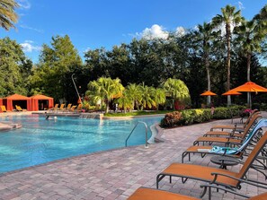 Area piscina con lettini e ombrelloni, circondata da palme e vegetazione.