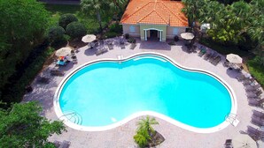 An aerial view of a swimming pool with lounge chairs and umbrellas, surrounded by palm trees and a building with a tiled roof. - Grand Resort 3BR Compass Townhouse Near Disney 1 (Kissimmee)