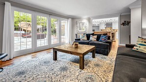 A spacious living room with a large window, a dark-colored sofa, a wooden coffee table, and a patterned rug. - Lighthouse | 9BR Resort · Pool · Arcade · Hot Tub (Saukville)