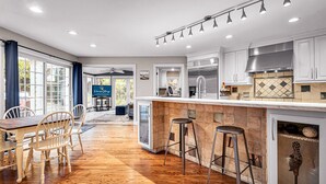 A modern kitchen with a wooden floor, white cabinets, a stainless steel range hood, and a bar area with stools. - Lighthouse | 9BR Resort · Pool · Arcade · Hot Tub (Saukville)