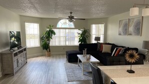 A spacious living room with a ceiling fan, a black sofa, a dining table, and two potted plants. - Disney Somerset 3BR Condo Near Theme Parks (Kissimmee)