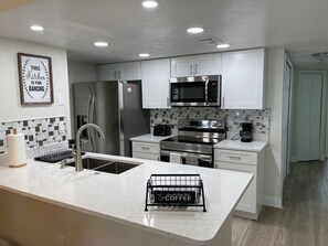 Una cocina moderna con gabinetes blancos, electrodomésticos de acero inoxidable y una zona de café.