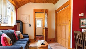 Un salon chaleureux avec un canapé bleu, une table basse en bois et un mur d’accent rouge. Une porte en bois donne accès à une autre pièce, et un tableau encadré est accroché au mur.