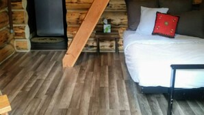 Un dormitorio de cabaña de madera con cama, mesita de noche, calentador y techo inclinado.