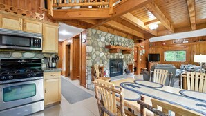 A spacious kitchen with a stone wall, wooden ceiling, and a dining area with rustic chairs.