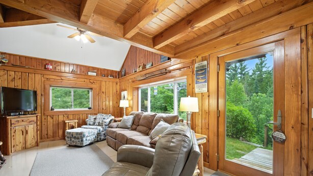 L’intérieur d’un chalet en bois, avec un canapé, un téléviseur et de grandes fenêtres donnant sur un paysage verdoyant.
