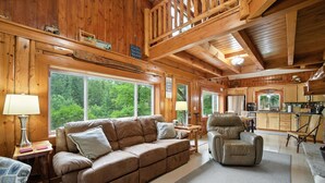 Un interior de cabaña acogedor, con techo de madera, un sofá, un sillón reclinable y una zona de cocina.
