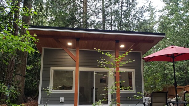 A modern cabin with a wooden deck, large windows, and a red umbrella. - Madrona Cabin 1-bedroom cabin in Sequim (Sequim)