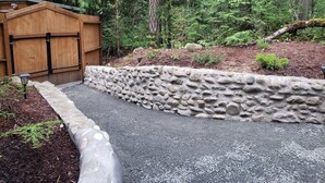 A stone retaining wall with a wooden gate, surrounded by a forested area. - Madrona Cabin 1-bedroom cabin in Sequim (Sequim)