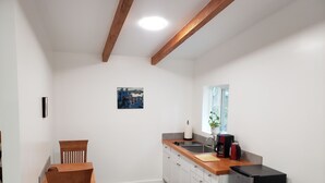 A compact kitchen with wooden beams, a dining area, and a window with a plant. - Madrona Cabin 1-bedroom cabin in Sequim (Sequim)