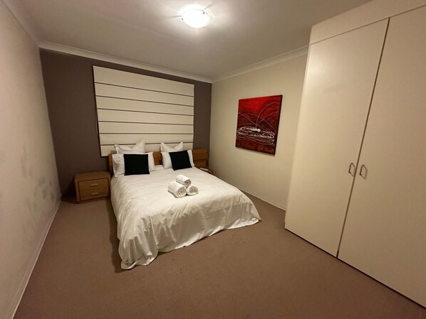 A neatly arranged bedroom with a bed, bedside tables, a wardrobe, and a piece of wall art.
