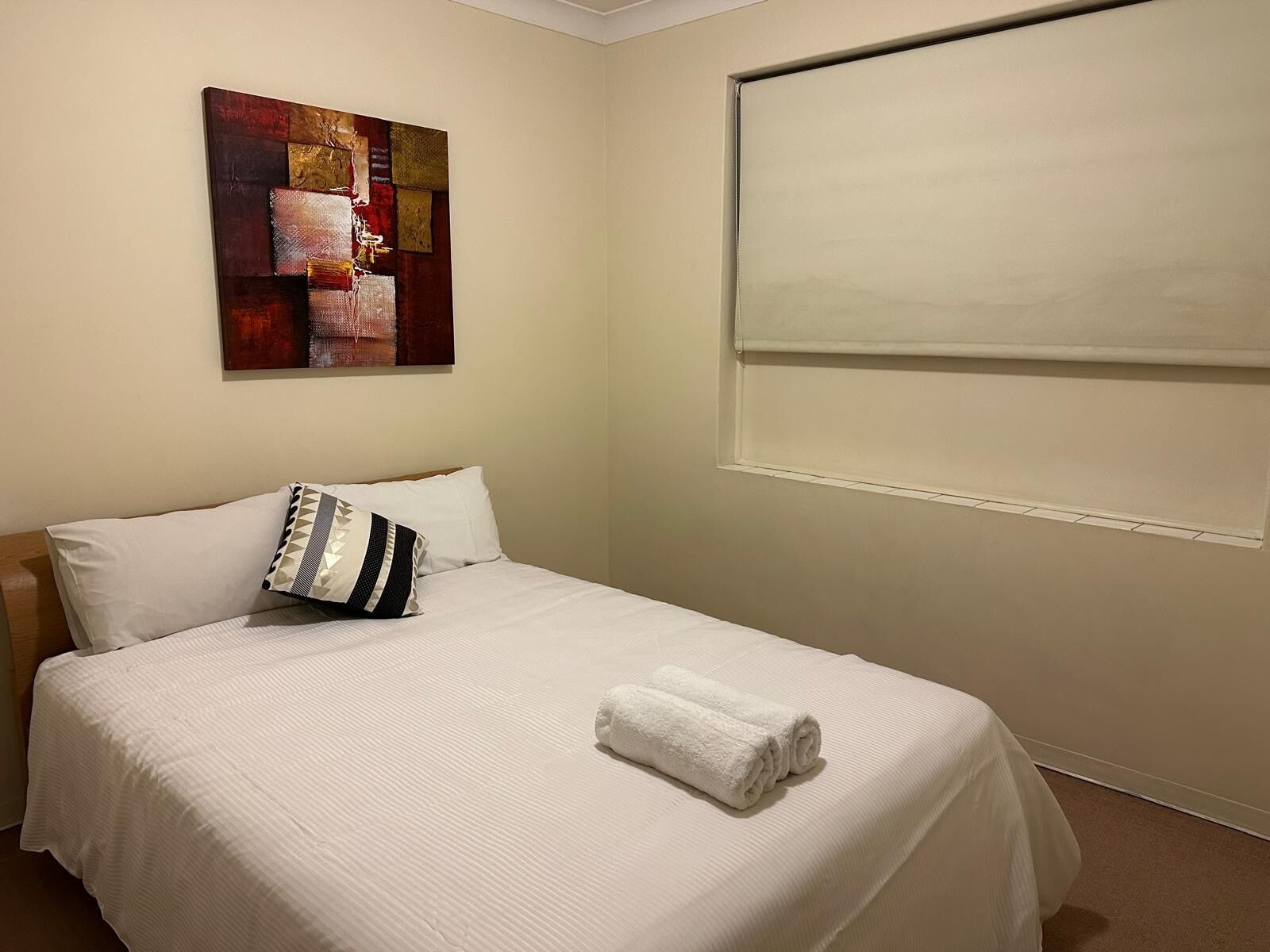Een net opgemaakt bed met witte lakens, een kussen met een geometrisch patroon en een opgerolde witte handdoek op het bed.