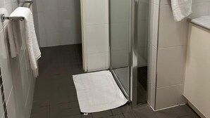 Ein kleines, schmales Badezimmer mit Duschabtrennung aus Glas, weißen Fliesen und einem Handtuchhalter.