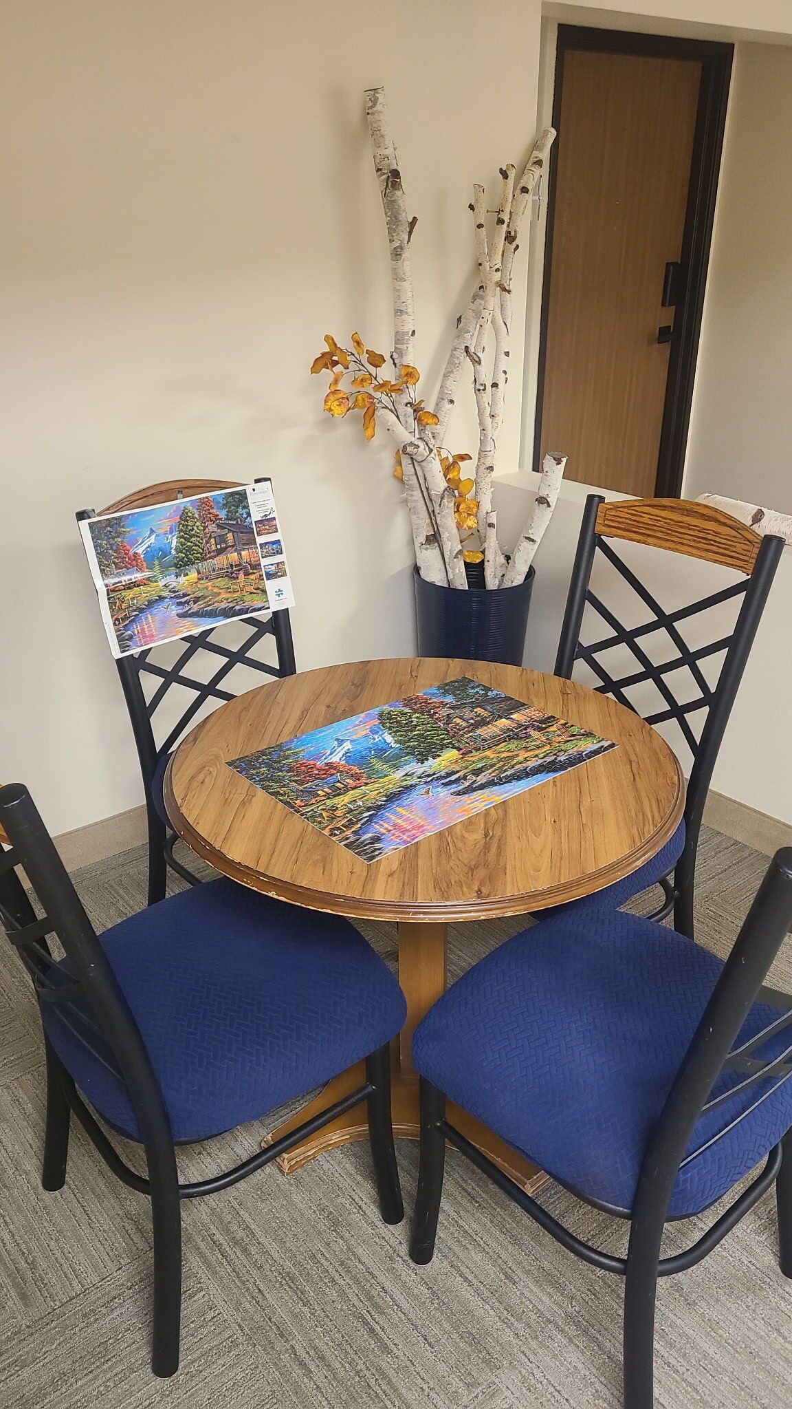 Een ronde houten tafel met een kleurrijk puzzelspel in het midden, omringd door blauwe fauteuils.