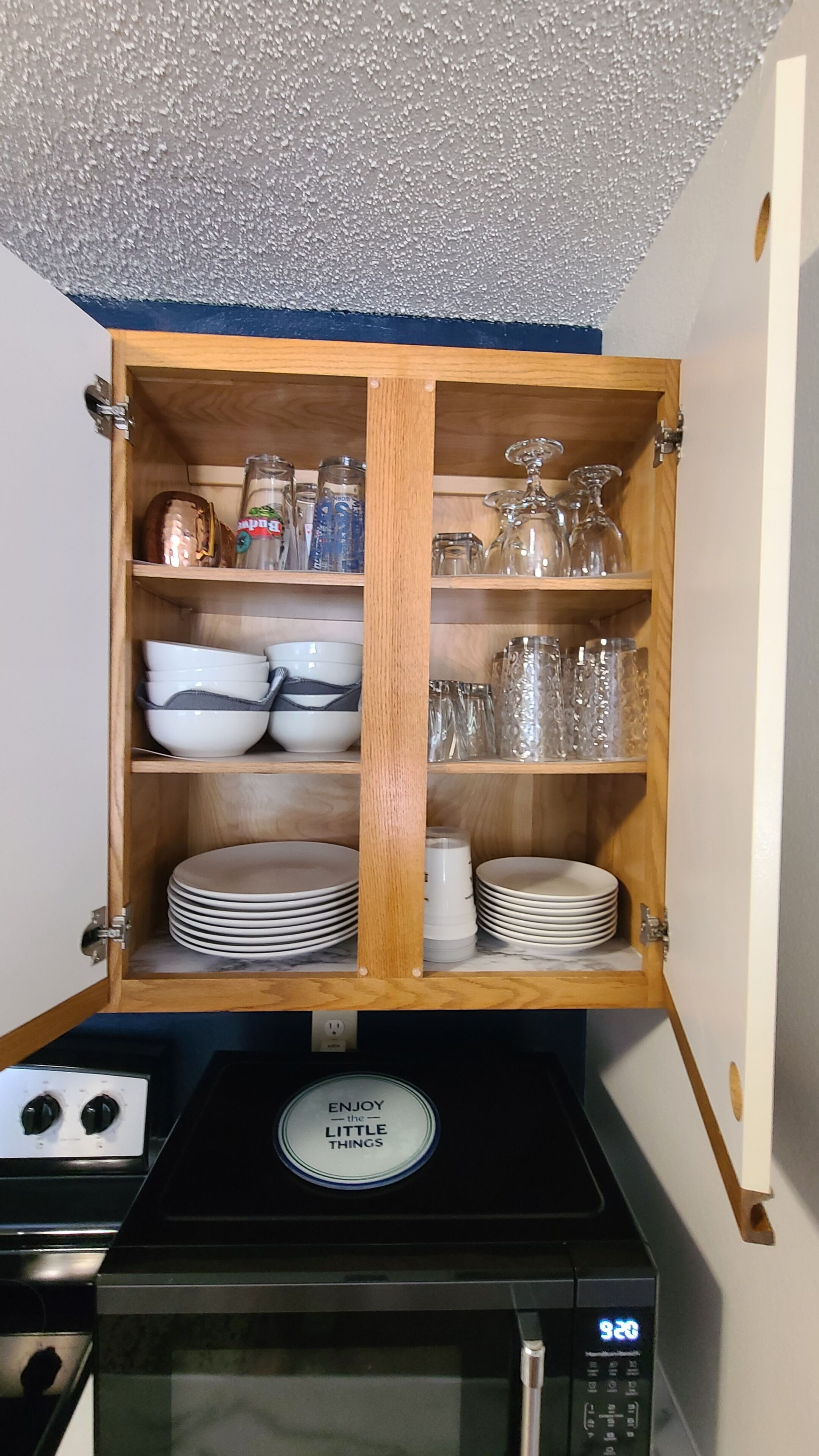 Een keuken met een houten kastje met servies, glazen en een magnetron.