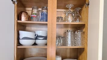 Een keuken met een houten kastje met servies, glazen en een magnetron.