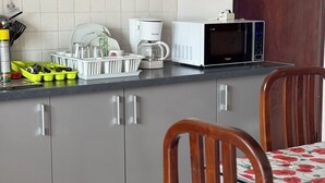 A kitchen with grey cabinets, a coffee maker, a microwave, and a dining table with chairs. - T3 cosy villa top 2 bedrooms (Les Abymes)