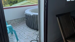 A room with a sliding glass door leading to a balcony with a patterned floor, a blue plastic chair, and a wooden rocking chair. - T3 cosy villa top 2 bedrooms (Les Abymes)