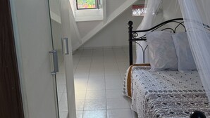 A bedroom with a bed, a window with a view, a door, and a ceiling with a sloped design. - T3 cosy villa top 2 bedrooms (Les Abymes)