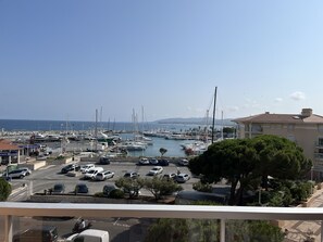 A marina with boats docked, a parking lot with cars, and a building with a balcony overlooking the marina. - Le Capitole, magnificent sea view, 1-bedroom apartment + cabin, 40m2, air conditioning and garage (Fréjus)