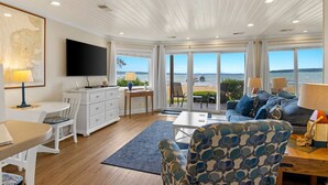 Amplia sala de estar con un gran ventanal con vista a la playa, un televisor de pantalla plana montado en la pared y un espacio de descanso cómodo con un sofá y sillones.