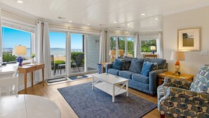 Un salón amplio con un sofá grande, una mesa de centro y vistas al mar a través de grandes puertas corredizas de vidrio.