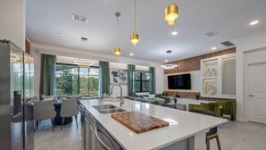 Una cocina moderna con una isla grande, electrodomésticos de acero inoxidable e iluminación colgante.
