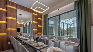 Un comedor moderno con una larga mesa dispuesta para una comida, ventanas amplias y un espejo que refleja la estancia.