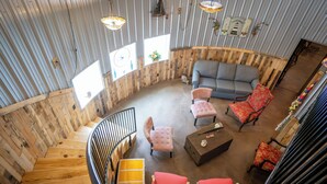 Spazioso loft con scala in legno, un divano grigio e poltrone rosse e rosa.