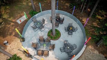 An outdoor patio area with multiple seating arrangements, including round and square tables, surrounded by chairs.