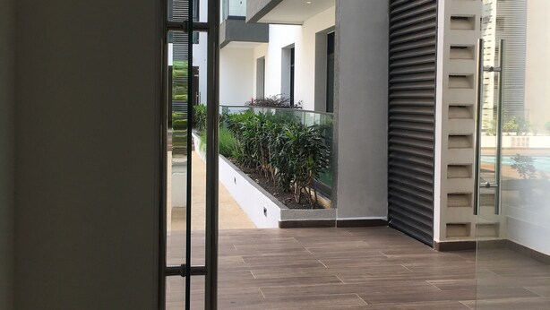 A modern interior with a glass door leading to an outdoor area, a tiled floor, and a view of a multi-story building with balconies.