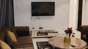 A modern living room with a flat-screen TV mounted on the wall, a coffee table with a vase of flowers, and two sofas.