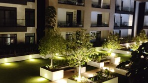 A modern building with multiple balconies and a well-lit courtyard with planters and trees.