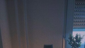 Una mesita de noche pequeña con una lámpara, un letrero de neón que dice "good vibes", y una planta en maceta sobre el alféizar de una ventana.