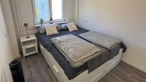 Un dormitorio con cama, mesitas de noche, una ventana y una lámpara en el techo.