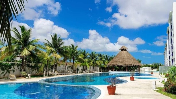 A resort with multiple swimming pools, palm trees, and a thatched-roof structure. - Deluxe 2 Bed 2 Bath Condo with a (Large outdoor Pool/Hot Tub) (Cancún)