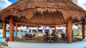 A covered outdoor area with a thatched roof, seating, and a pool. - Deluxe 2 Bed 2 Bath Condo with a (Large outdoor Pool/Hot Tub) (Cancún)