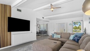 Un salon moderne avec un canapé d’angle, un téléviseur à écran plat et un ventilateur de plafond.
