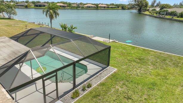 Une piscine extérieure moderne, dotée d’une structure en verre, entourée d’une pelouse bien entretenue et offrant une vue sur un lac.