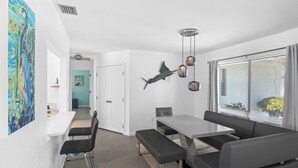 Un espace repas moderne avec une table blanche, des chaises noires et un banc. Un poisson décoratif orne le mur, et un luminaire est suspendu au plafond.