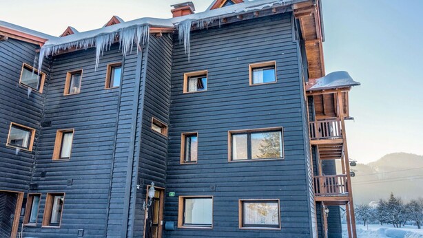 Un bâtiment en bois à plusieurs étages, dont le toit est recouvert de neige et orné de glaçons.