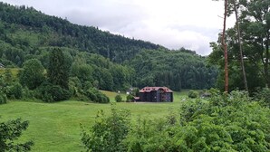 Une maison de campagne avec un toit rouge, entourée d’une végétation luxuriante et de collines.