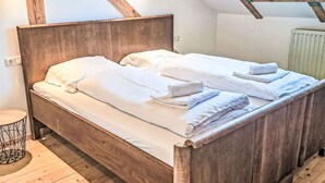 Un lit en bois avec du linge de lit et des serviettes blanches, une petite table ronde et une lucarne au-dessus.