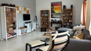 A living room with a sofa, armchairs, a coffee table, a bookshelf, a TV, and a painting.