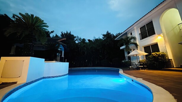 A swimming pool with a tiled edge, surrounded by a white wall and a building with a balcony.