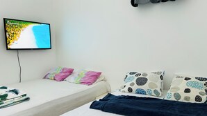 A hotel room with two beds, a TV on the wall, and a view of a beach.