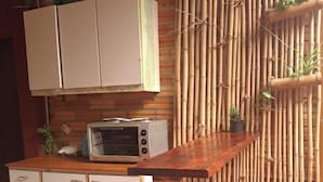 A kitchen with a microwave, cabinets, and a bamboo wall. - Bungalow hostel Iguazù (Puerto Iguazú)